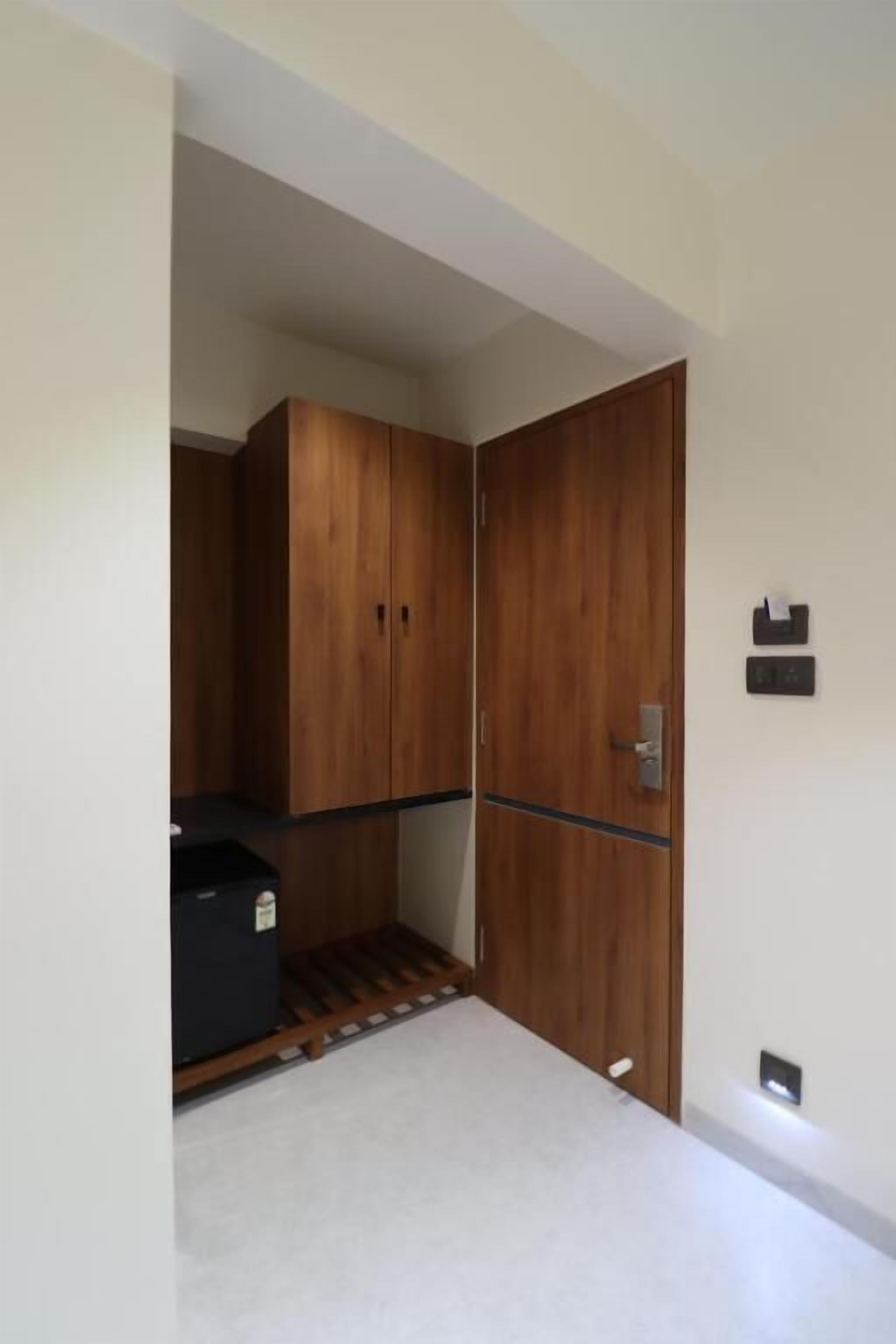 A room with a wooden wardrobe, a small black object on the floor, and a wall-mounted light switch.
