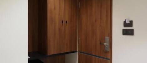 A room with a wooden wardrobe, a small black object on the floor, and a wall-mounted light switch.