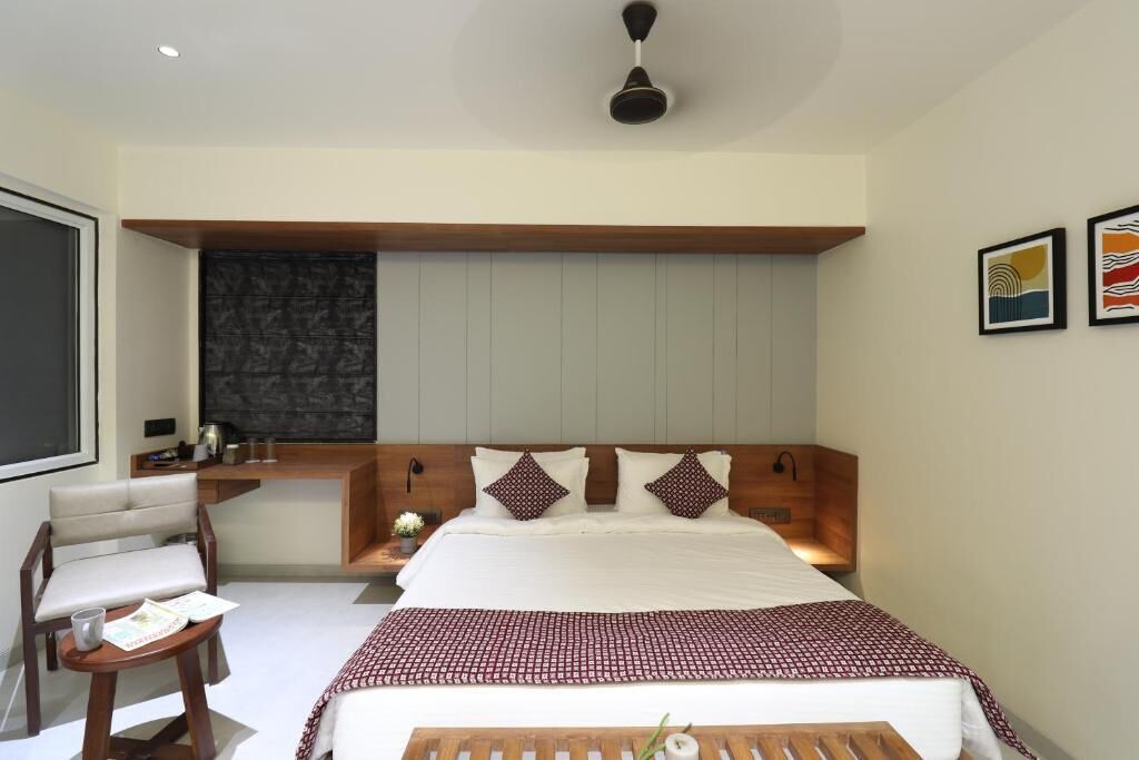 A modern hotel room with a large bed, a desk, a chair, and a small table.