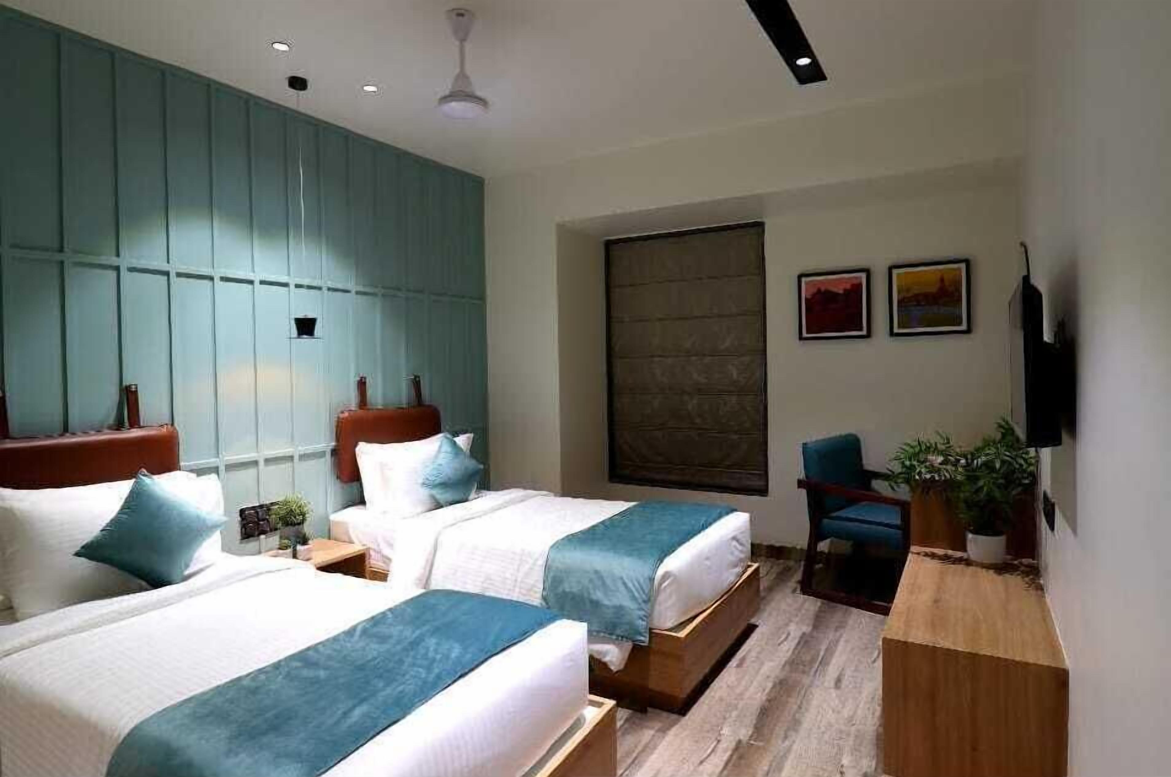 Een hotelkamer met twee bedden, een bureau, een stoel, een televisie en een raam met jaloezieën.