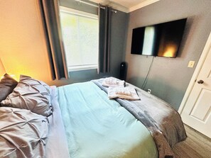 Ein Schlafzimmer mit einem Bett, einem flachbildfernseher an der Wand und einem Fenster mit Vorhängen.