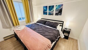 A neatly made bed with a pink blanket, a black and gray duvet, and a white pillow. There are three framed pictures on the wall above the bed.