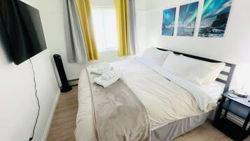 A hotel room with a bed, a flat-screen TV mounted on the wall, a window with curtains, and artwork on the wall.