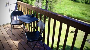 A wooden deck with two chairs and a table, overlooking a grassy yard with trees and a building in the background.