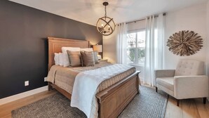 A bedroom with a wooden bed, a chandelier, a window with curtains, and a decorative wall piece.