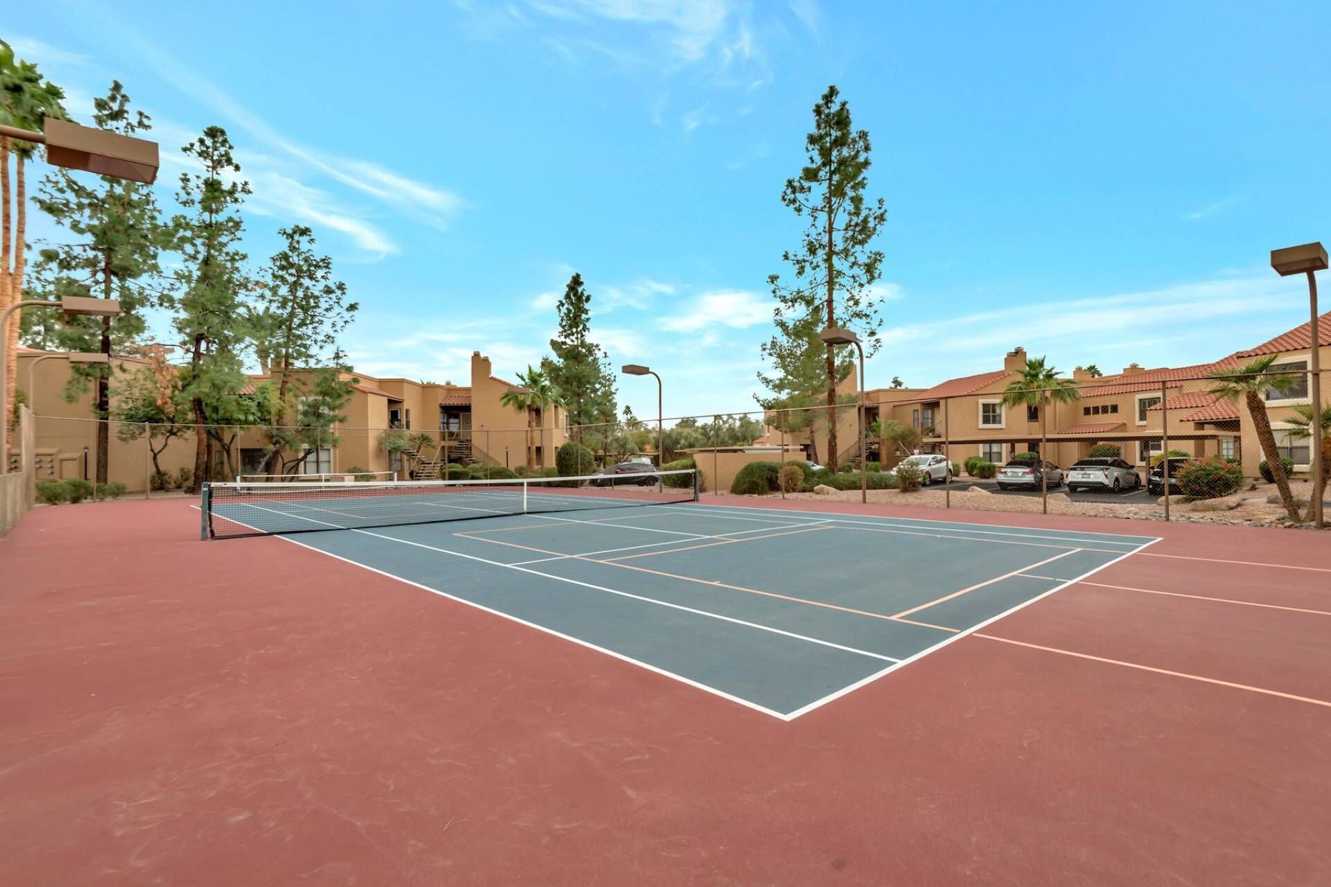 A tennis court with a net, surrounded by trees and buildings.