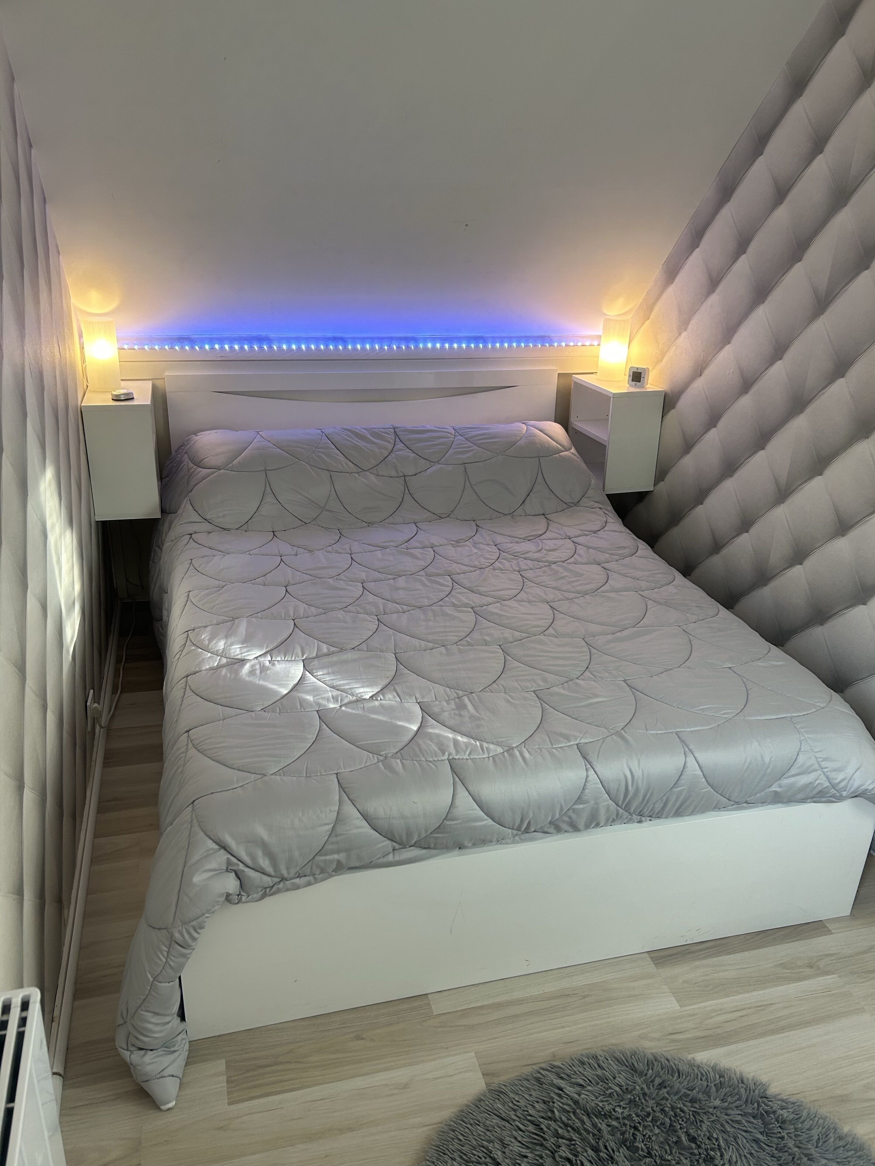 Ein Schlafzimmer mit einem Bett, Nachttischen und einem Kopfteil mit LED-Beleuchtung.