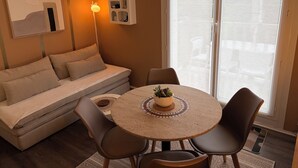 A modern living room with a sofa, a round table with chairs, a floor lamp, and a large window with blinds. - Pleasant duplex, direct access, free wifi beach  (Merville-Franceville-Plage)