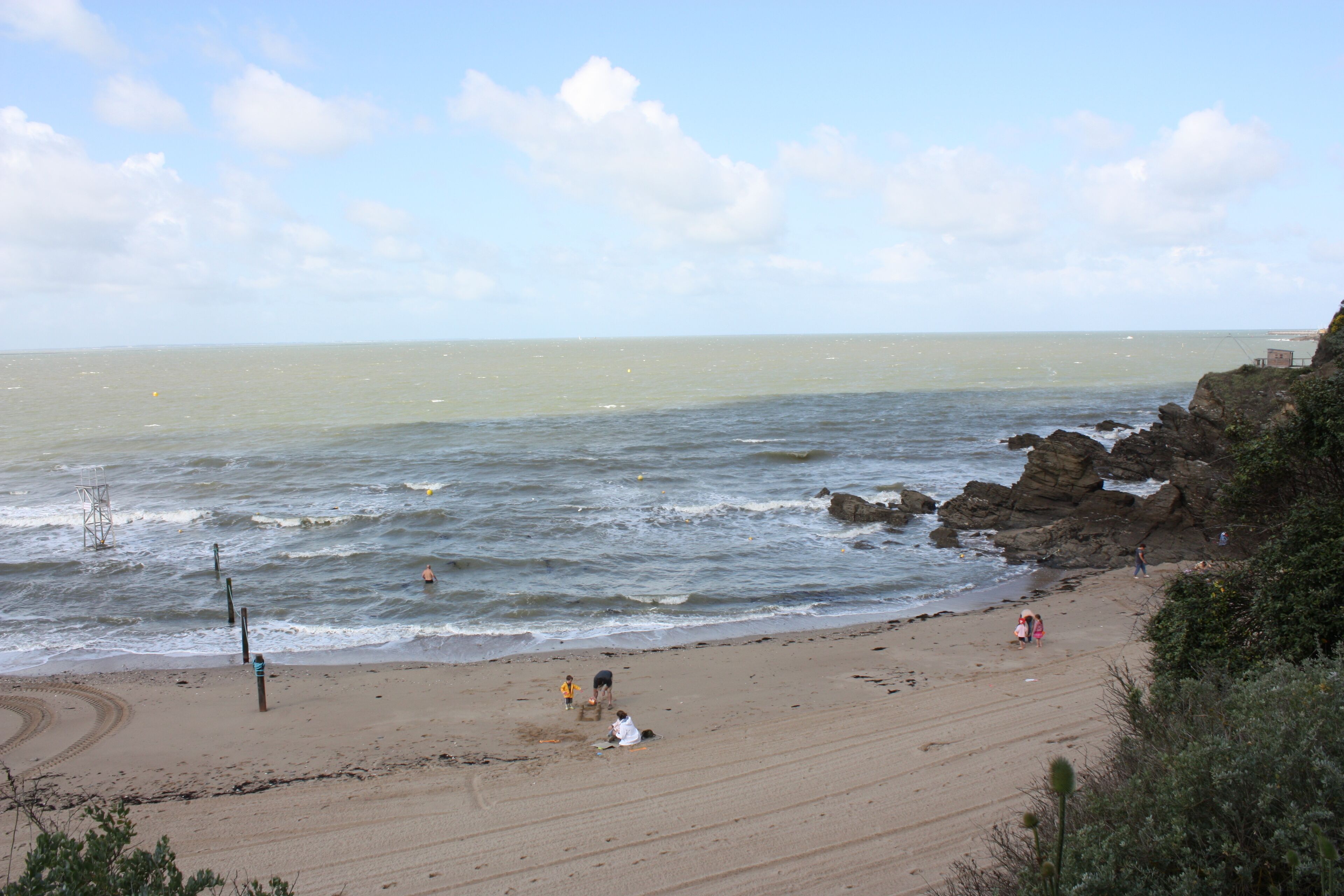 A beach with rocky cliffs, calm sea, and a few people walking.