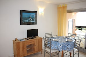 Ein Essbereich mit einem für vier Personen gedeckten Tisch, einem Fernseher auf einer Holzkommode und einem gerahmten Bild eines Leuchtturms an der Wand.