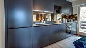 A modern kitchen with dark cabinetry, a built-in oven, and a large window providing natural light. - Appartement Mont Parrain 2627 with Sauna - La Tzoumaz, 4 Vallees (La Tzoumaz)