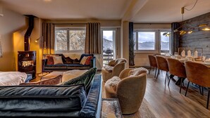 A cozy living room with a fireplace, a dining area with a wooden table and chairs, and large windows offering a mountain view. - Appartement Mont Parrain 2627 with Sauna - La Tzoumaz, 4 Vallees (La Tzoumaz)