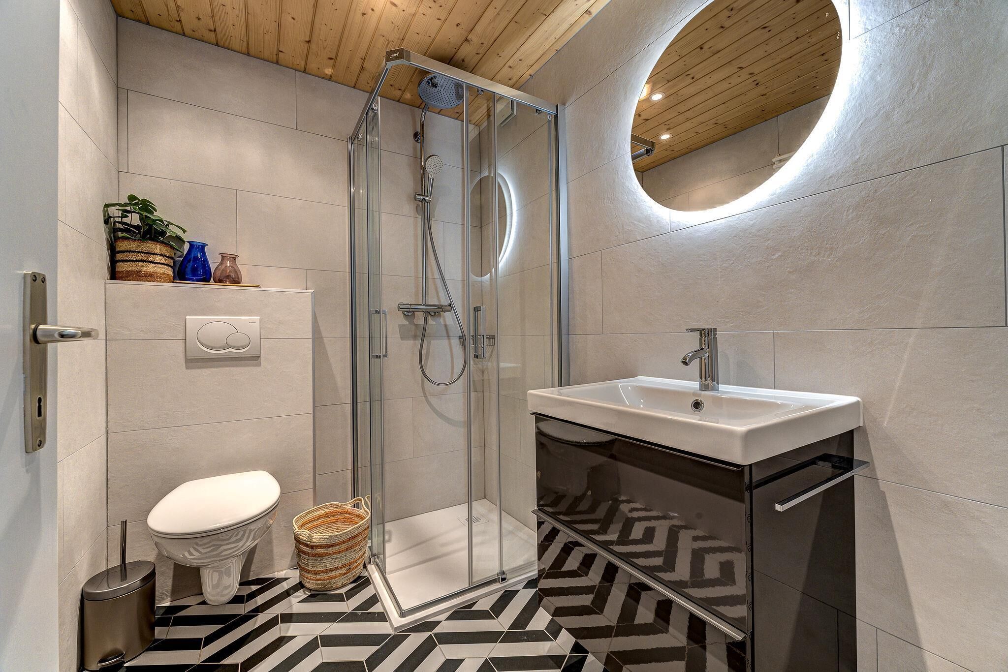 A modern bathroom with a glass-enclosed shower, a white toilet, and a black and white patterned floor.