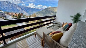 A balcony with a sofa and a small table, overlooking a mountainous landscape with buildings in the distance. - Appartement Mont Parrain 2627 with Sauna - La Tzoumaz, 4 Vallees (La Tzoumaz)