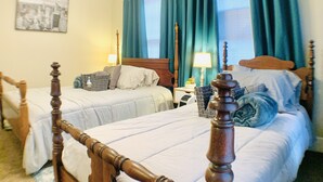 A hotel room with two beds, a wooden headboard, a nightstand with a lamp, and a window with curtains.