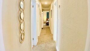 A hallway with white walls, a beige carpet, and a decorative gold mirror on the left.