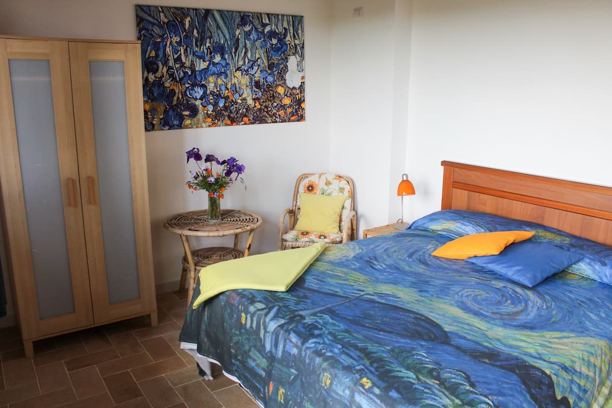 Ein Schlafzimmer mit einem Bett, einem Sessel, einem kleinen Tisch mit einer Vase und einem Kleiderschrank.