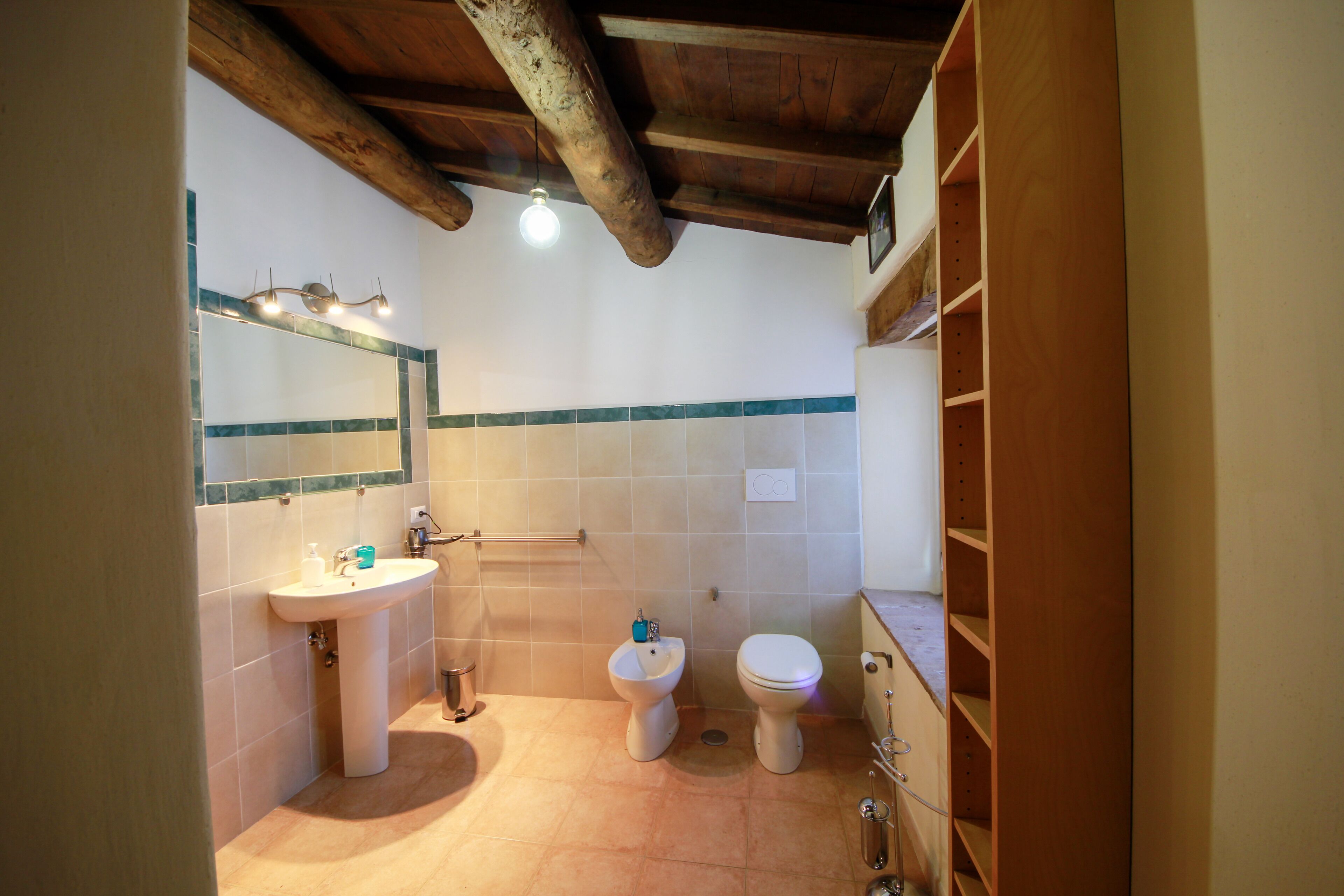 A bathroom with a sink, two toilets, a mirror, and wooden shelving.