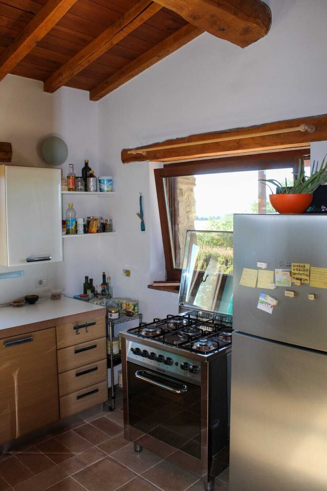 A kitchen with a gas stove, a refrigerator, wooden cabinets, and a window with a view.