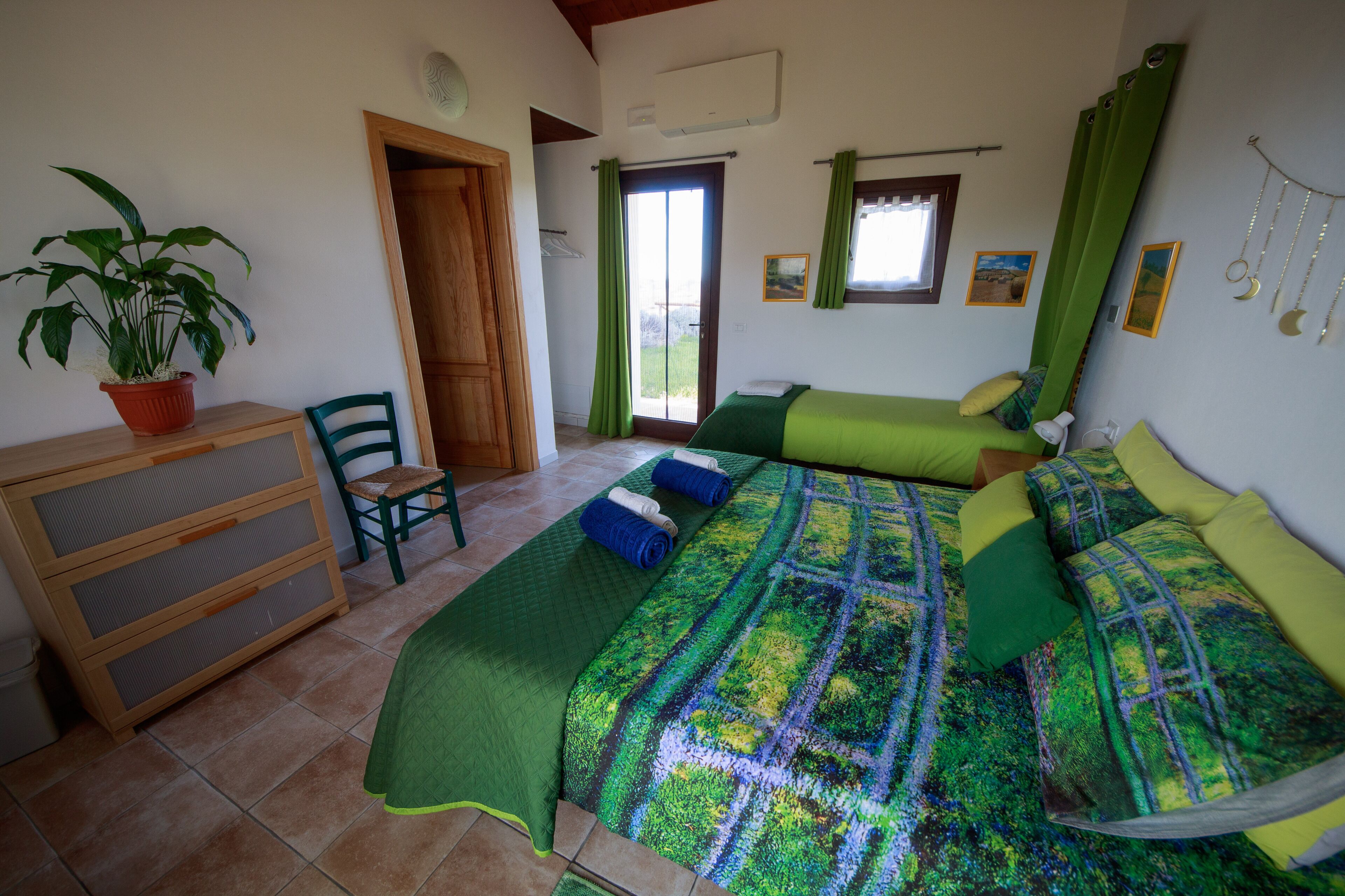 A bedroom with two beds, a wooden dresser, a chair, a potted plant, and a window with curtains.
