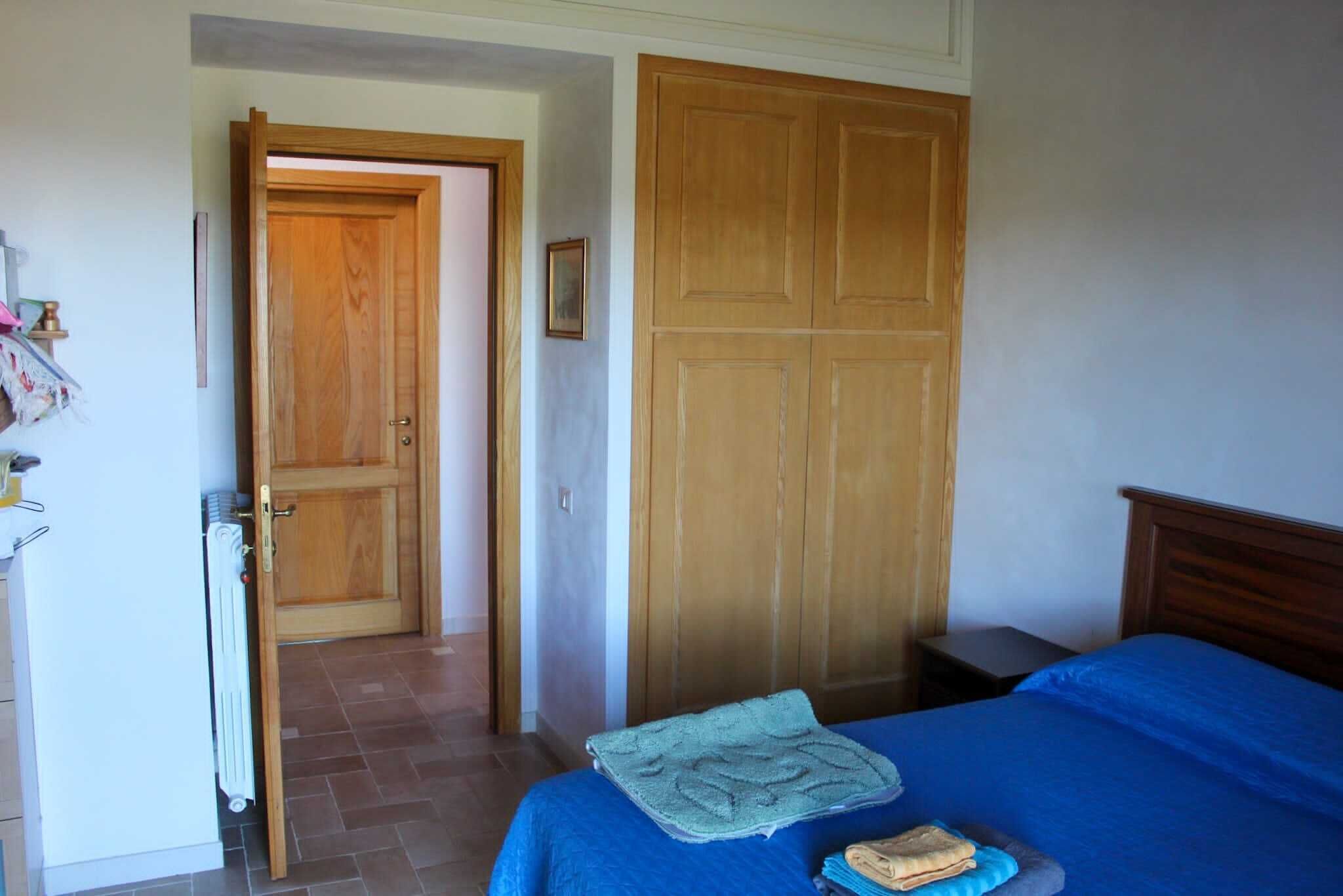 Un dormitorio con cama, armario de madera, radiador y puerta que da a otra habitación.