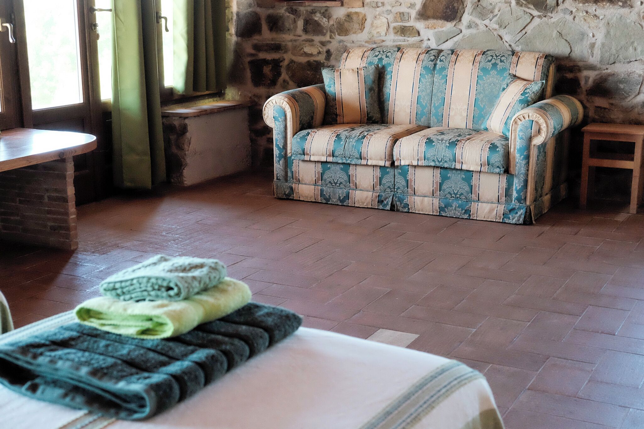 A cozy room with a patterned sofa, a small wooden table, and a bed with neatly folded blankets.