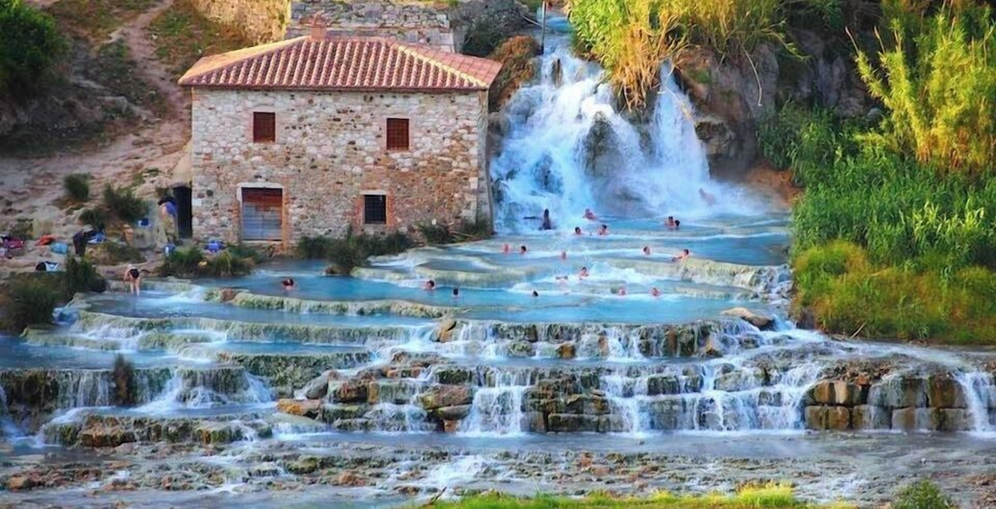 A stone building with a tiled roof, a series of terraced pools, and a waterfall.