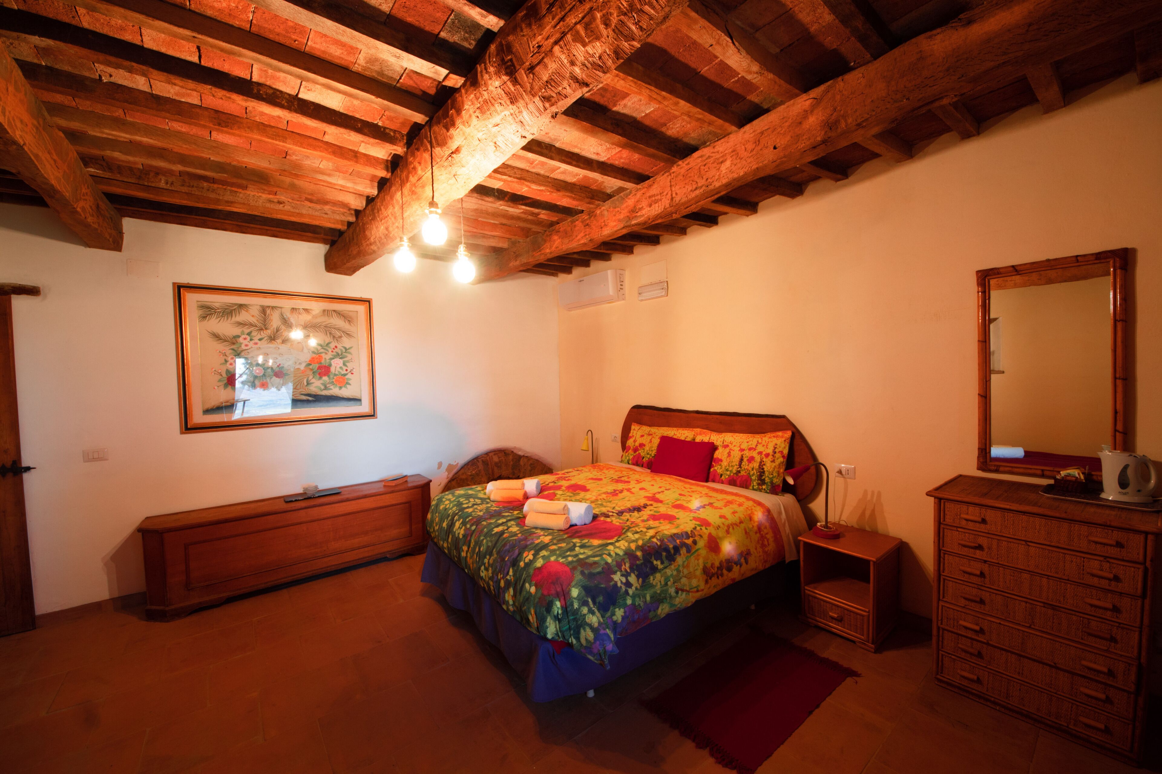 A bedroom with a wooden ceiling, a bed with floral bedding, a nightstand, a dresser, and a mirror.