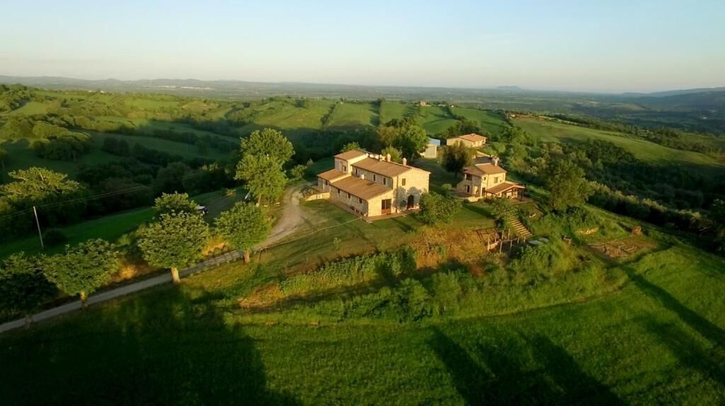 A rural property with multiple buildings surrounded by lush green fields and rolling hills.