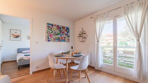Un coin repas avec une table ronde, des chaises blanches, un tableau abstrait aux couleurs vives et une vue dégagée grâce à de grandes fenêtres.