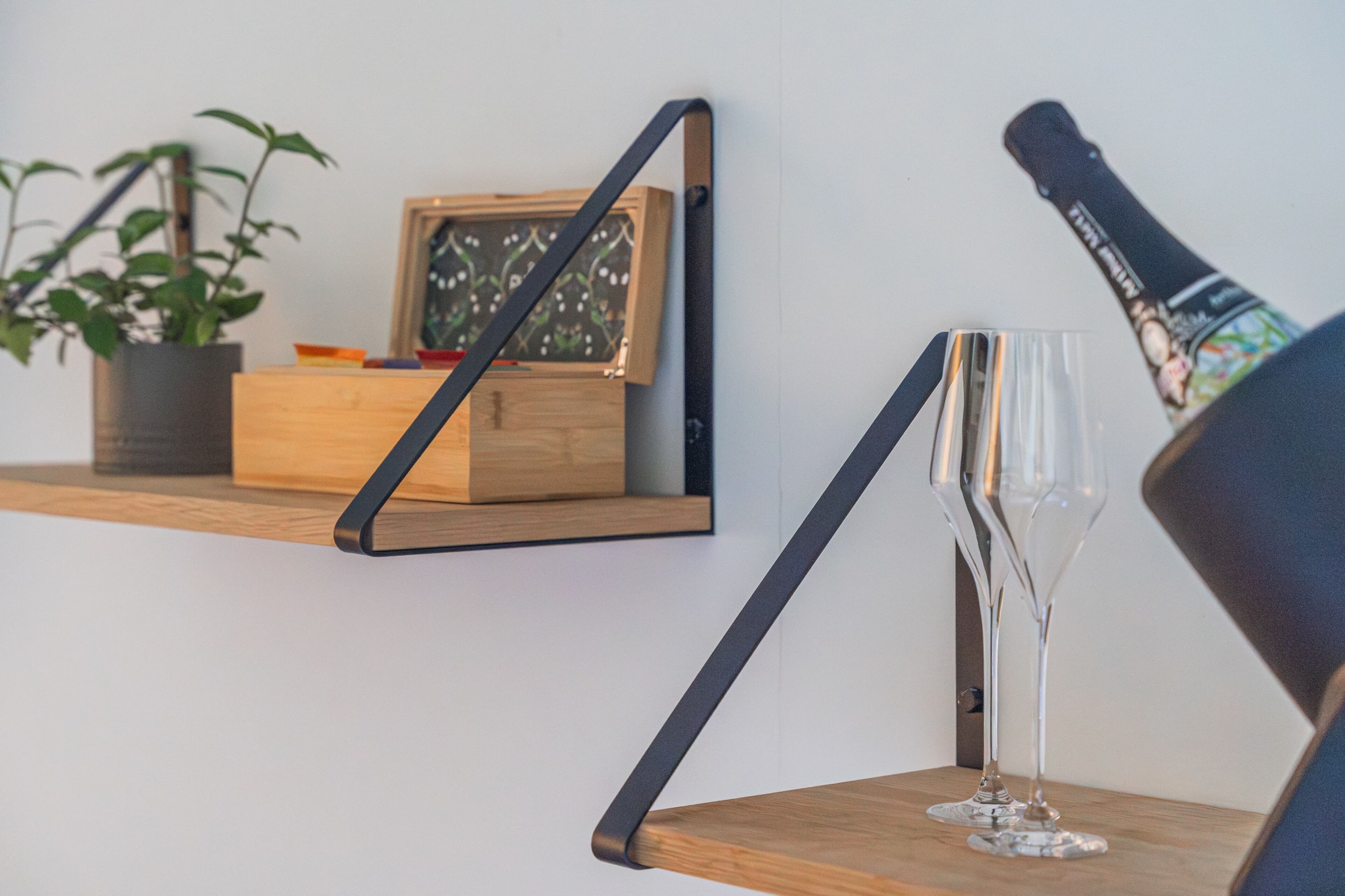 Uno scaffale di legno con un quadro incorniciato, una pianta in vaso e una flûte di champagne su un tavolo.