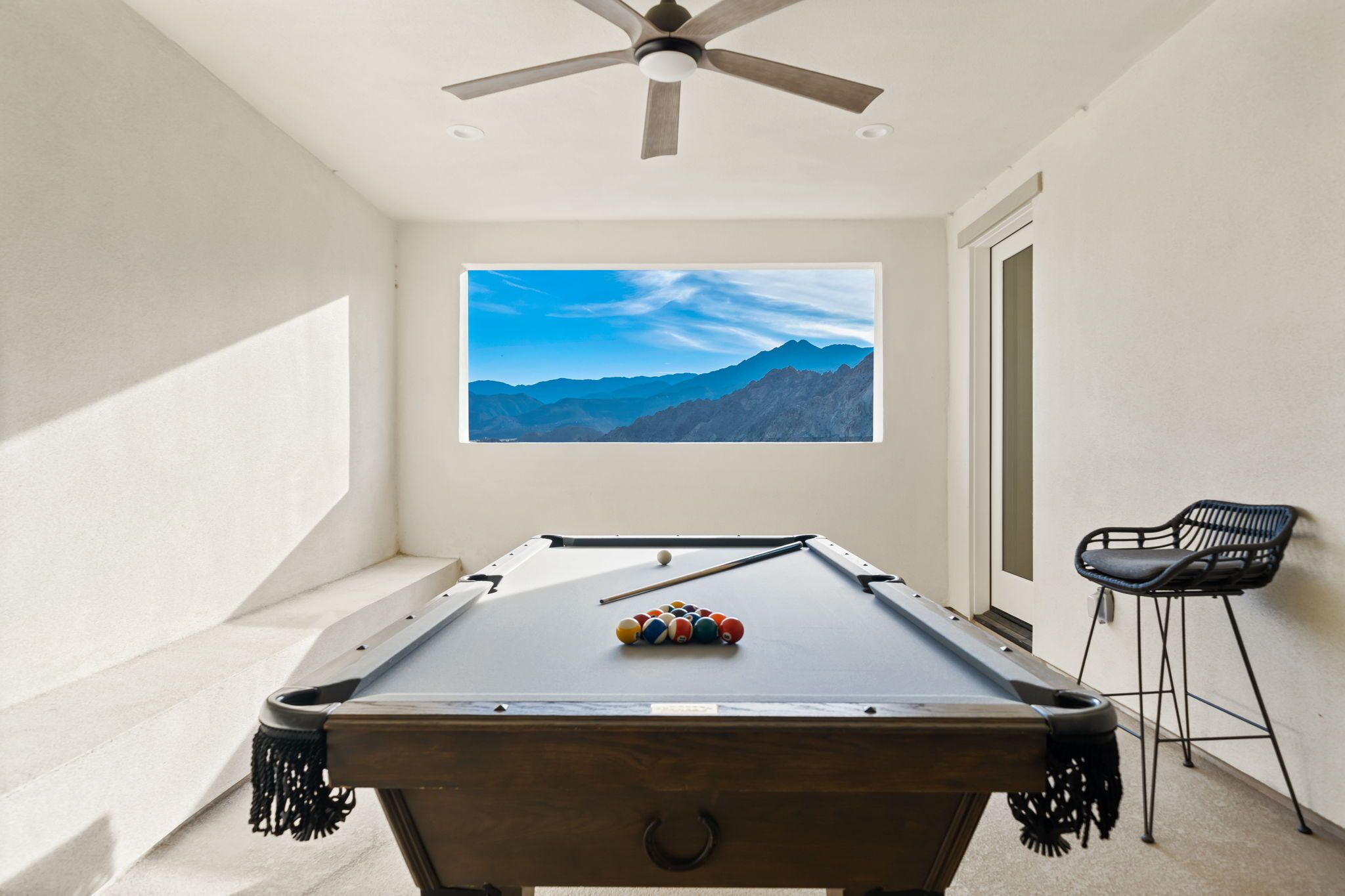 A pool table with a mountain view, a ceiling fan, and a bar stool.