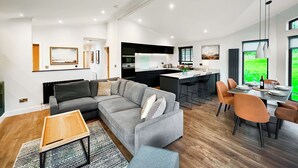 Ein modernes Wohnzimmer mit einem grauen Ecksofa, einem Holztisch und einem Essbereich mit orangefarbenen Stühlen.