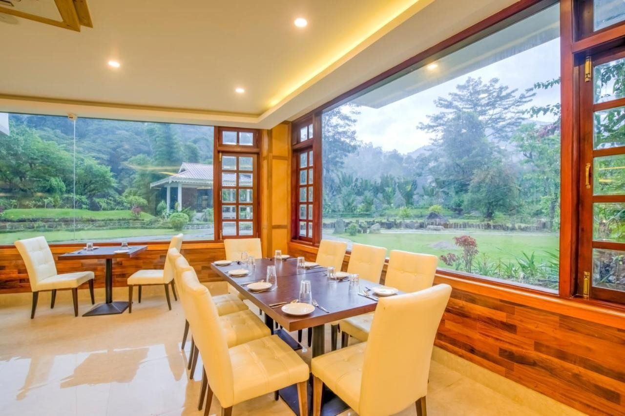 Un comedor con una mesa larga y sillas, ventanas amplias con vista a un jardín.