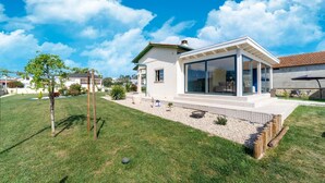 A modern house with a glass-enclosed patio, surrounded by a well-maintained lawn and a small garden. - Rustic Spa Retreat in Netos (Netos  Almagreira)
