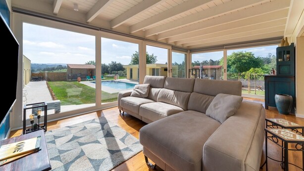 A spacious living room with a large sectional sofa, a coffee table, and a view of a swimming pool and garden. - Rustic Spa Retreat in Netos (Netos  Almagreira)