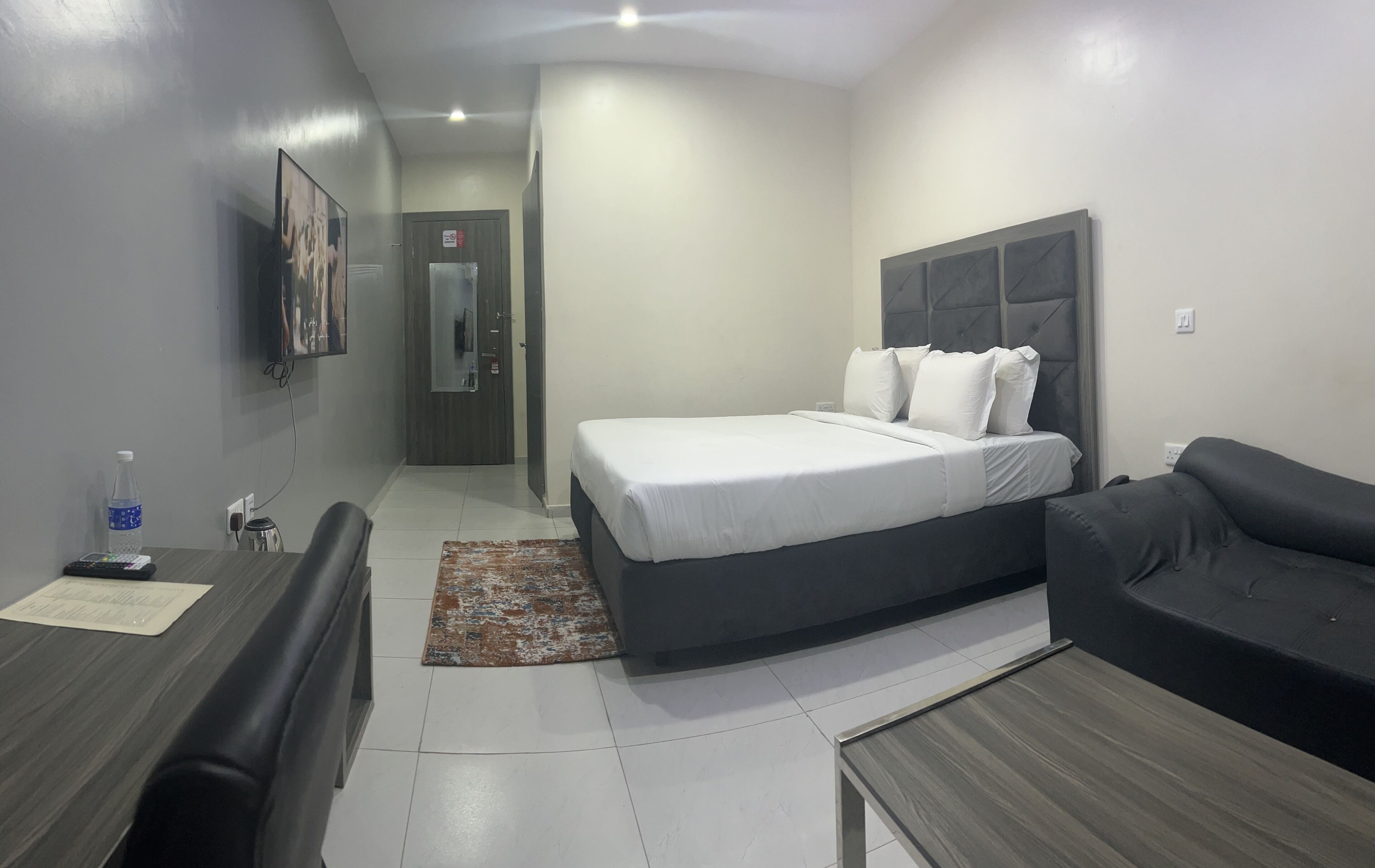 A modern hotel room with a bed, a sofa, a desk, and a TV.