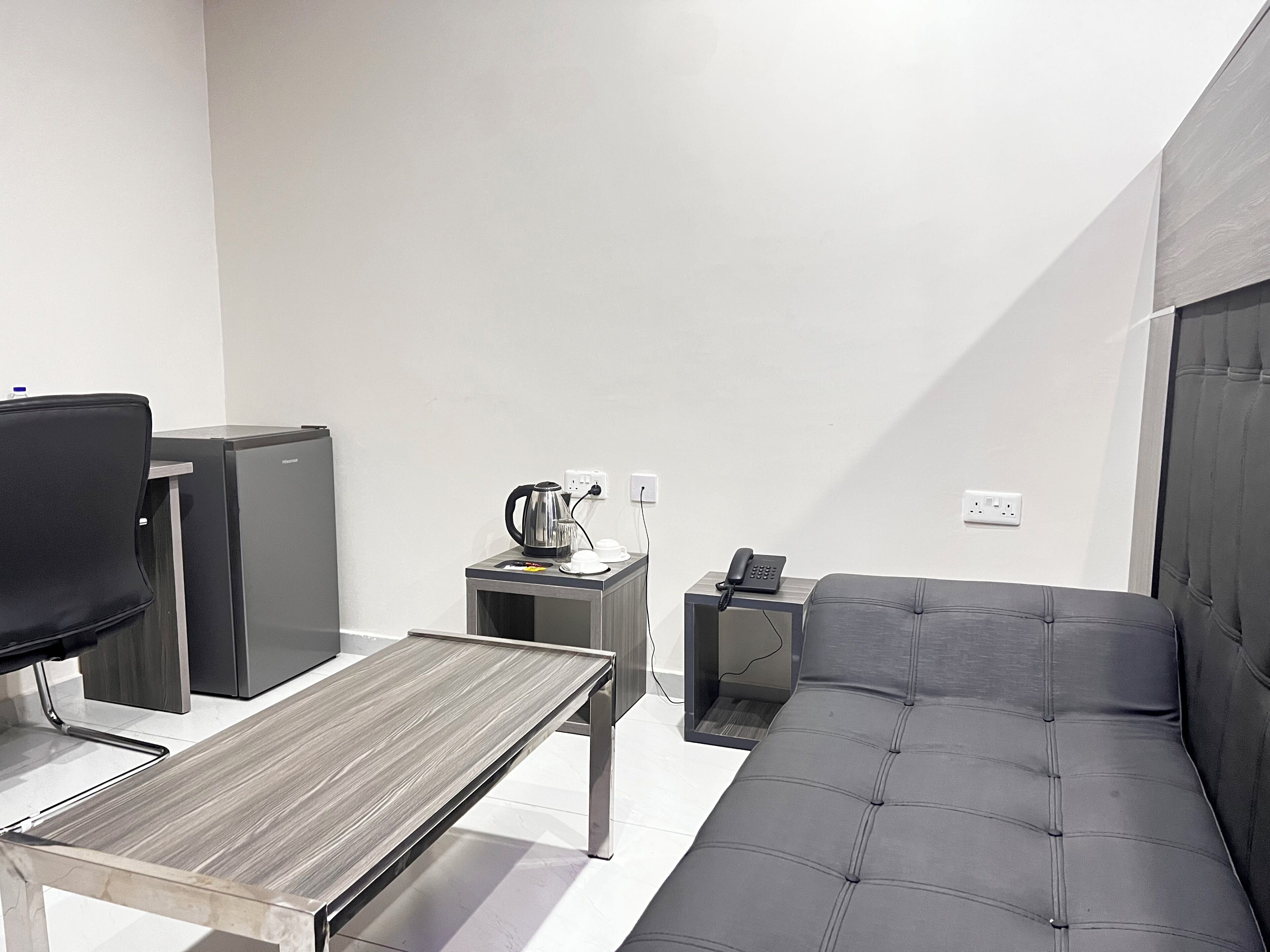 A modern room with a sofa, a small table, a TV, a coffee maker, and a phone on a side table.