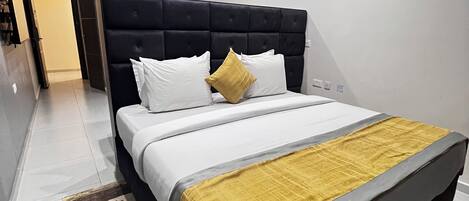 A modern bedroom with a black headboard, white bedding, and a yellow throw.