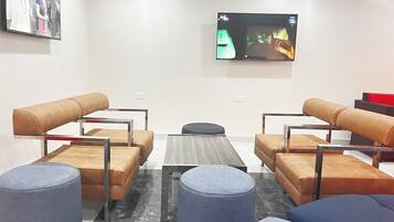A modern lounge area with leather sofas, round ottomans, and a flat-screen TV mounted on the wall.