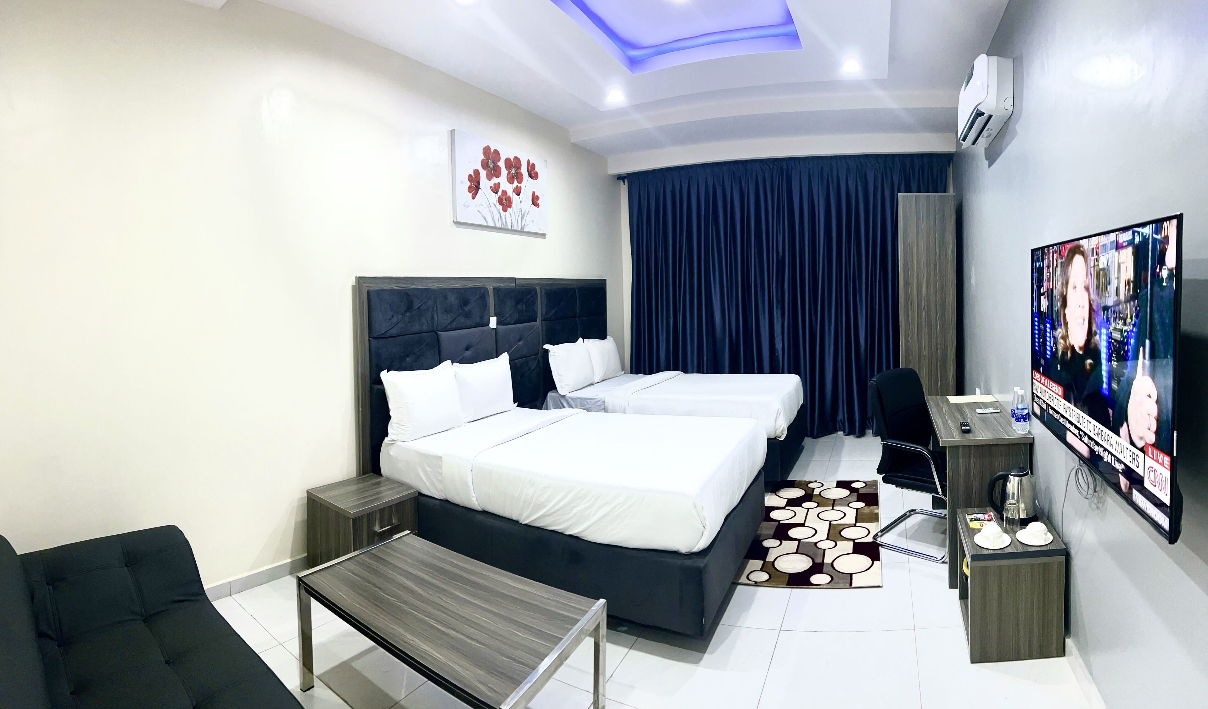 A hotel room with a large bed, two bedside tables, a desk, a chair, a TV, and a ceiling light.