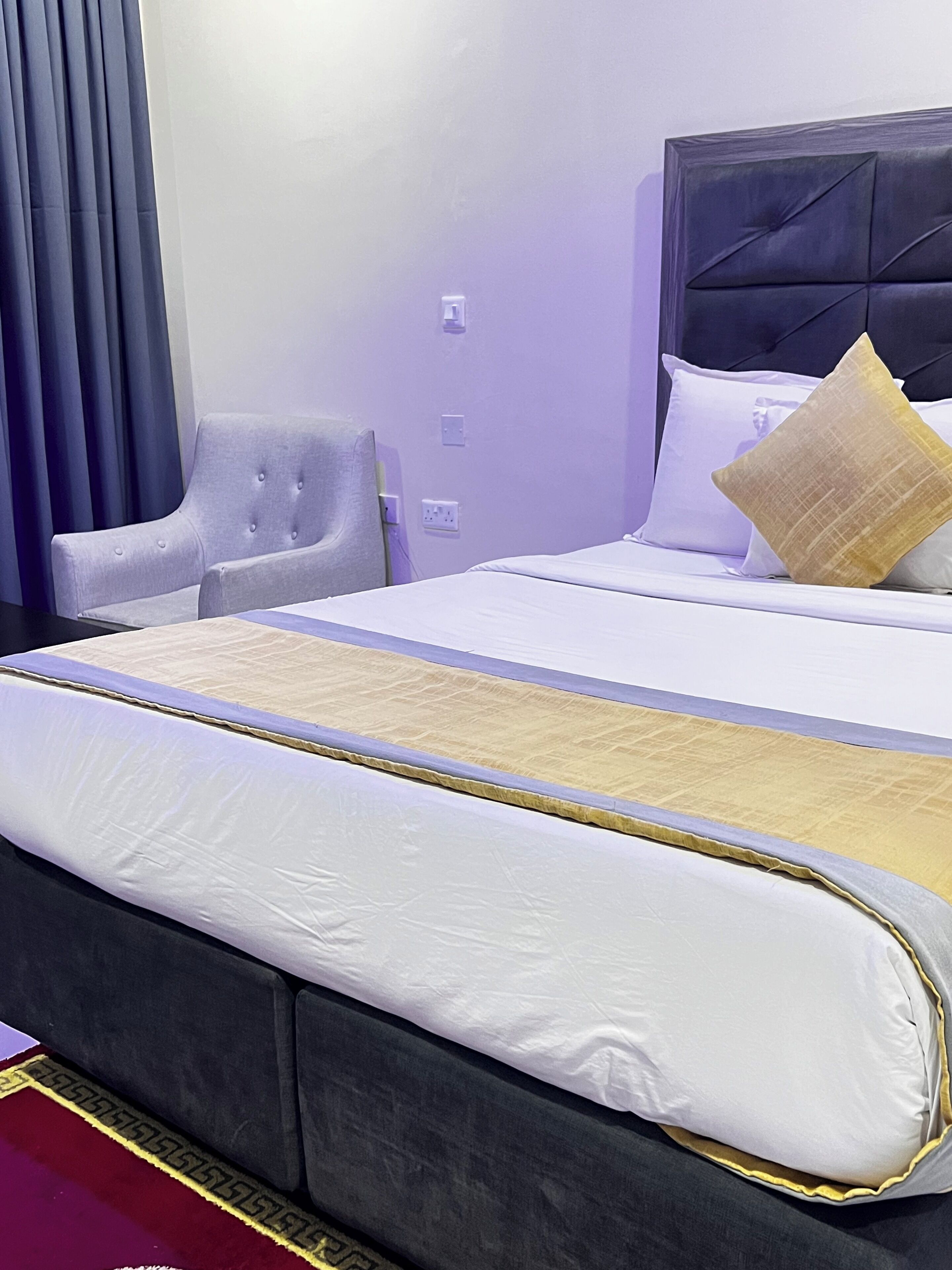 A hotel room with a large bed, a grey upholstered chair, and a headboard with a tufted design.