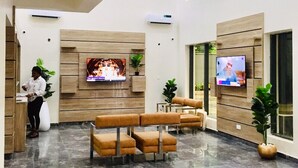 A lobby with a reception desk, seating area, and two televisions mounted on the walls. - De Rigg Place Victoria Island  (Lagos)