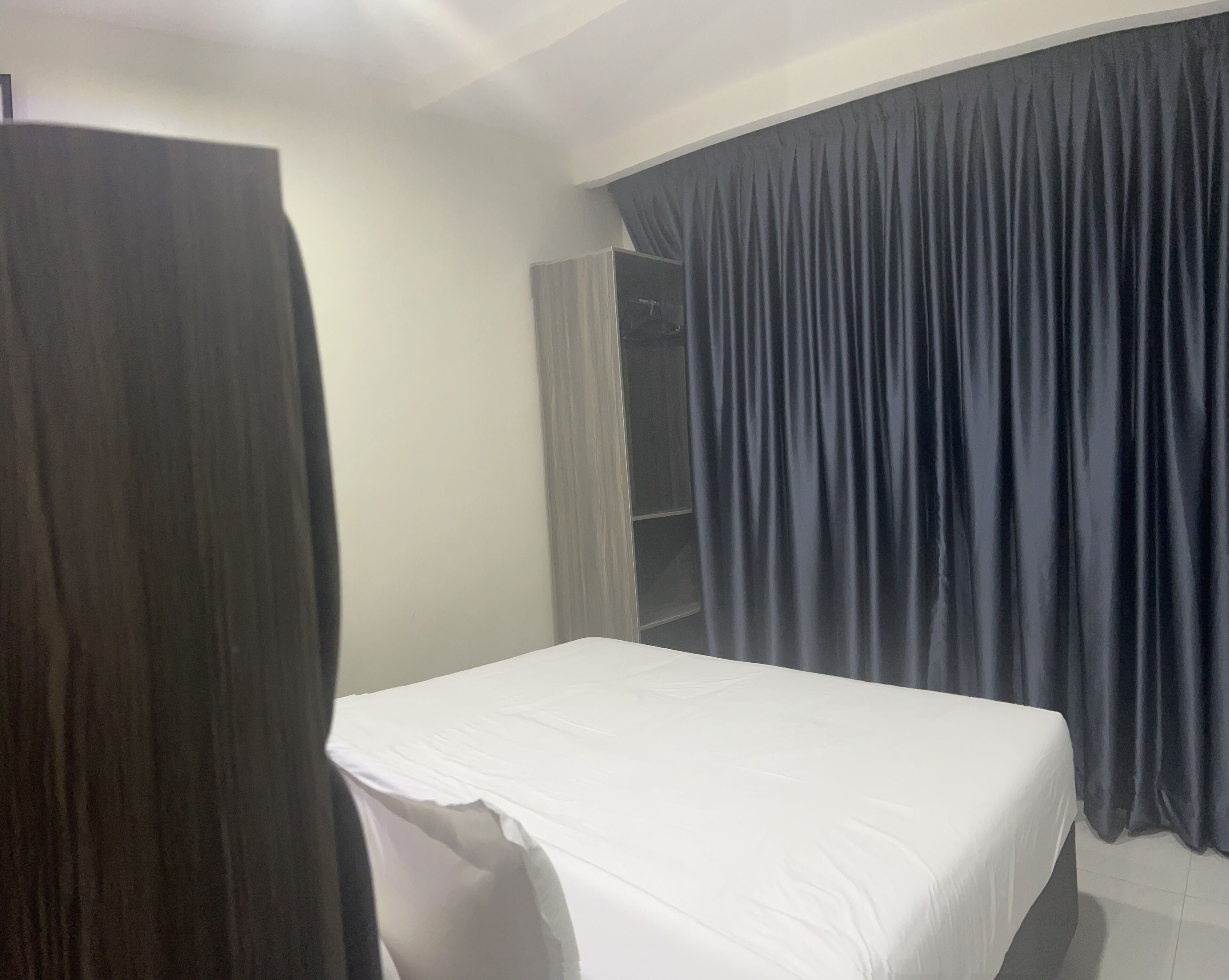Una habitación de hotel con cama, armario y cortina.