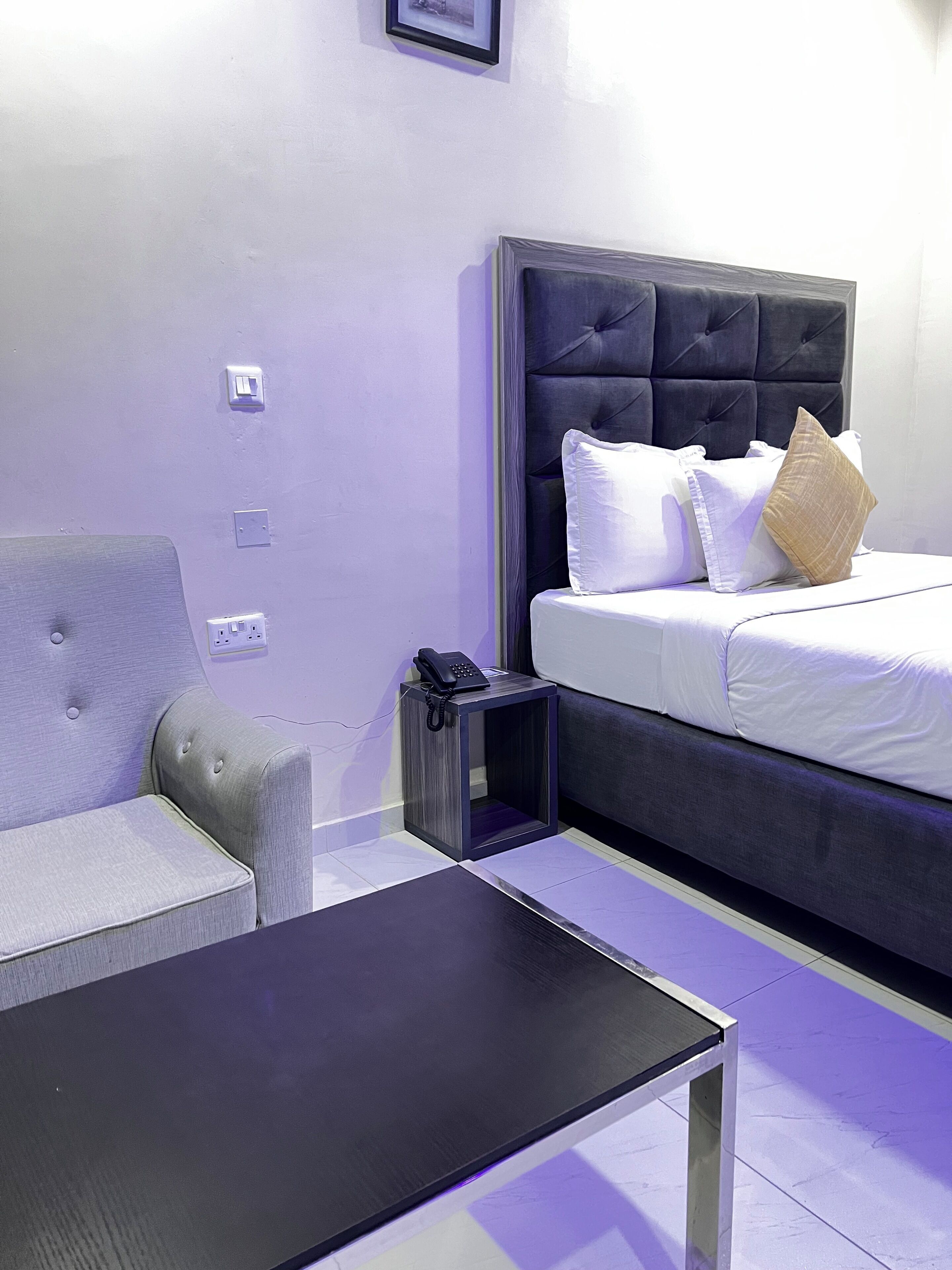 Ein Hotelzimmer mit einem Bett, einem grauen Sofa, einem kleinen Tisch und einem Nachttisch mit einem Telefon.