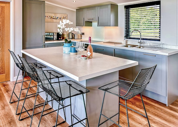 A modern kitchen with a central island, bar stools, and a window with blinds.