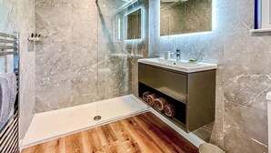 A modern bathroom with a glass-enclosed shower, a vanity with a mirror, and a wooden floor. - Royal Forest Pet Friendly Lodge (Coleford)