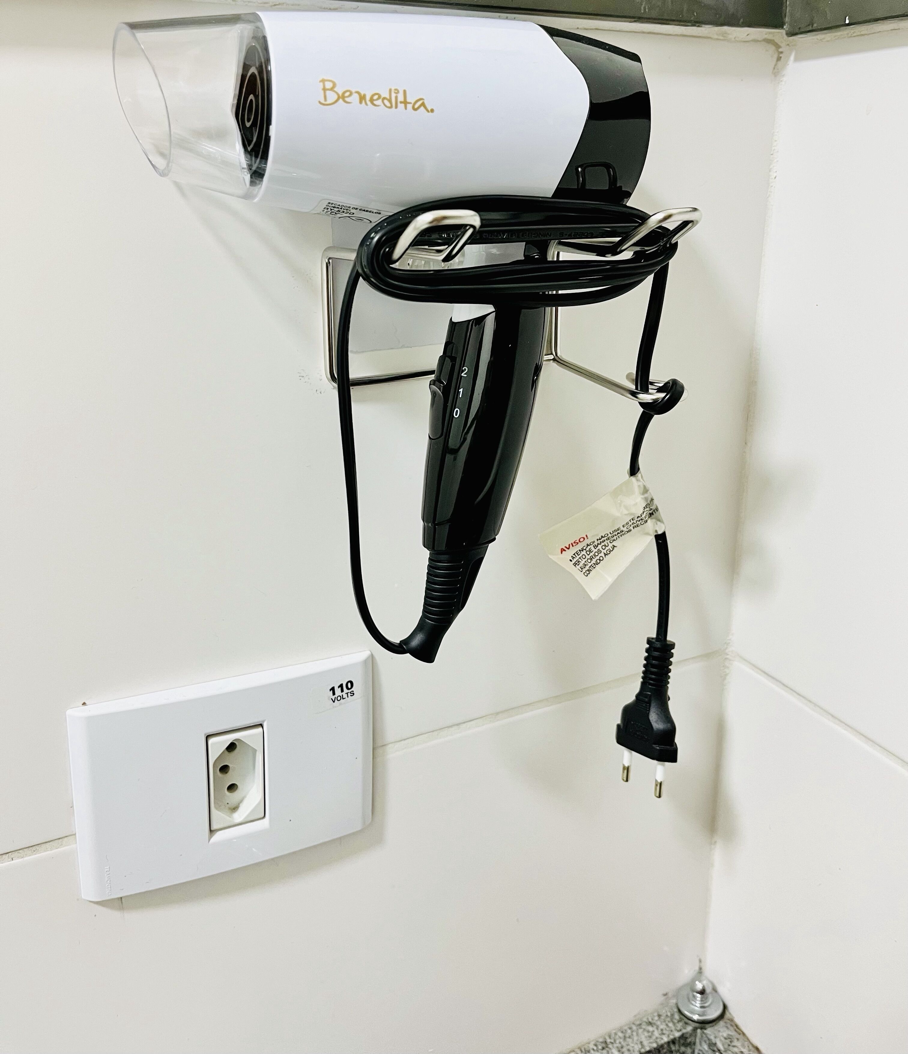 A hair dryer mounted on a wall with a power outlet below it.