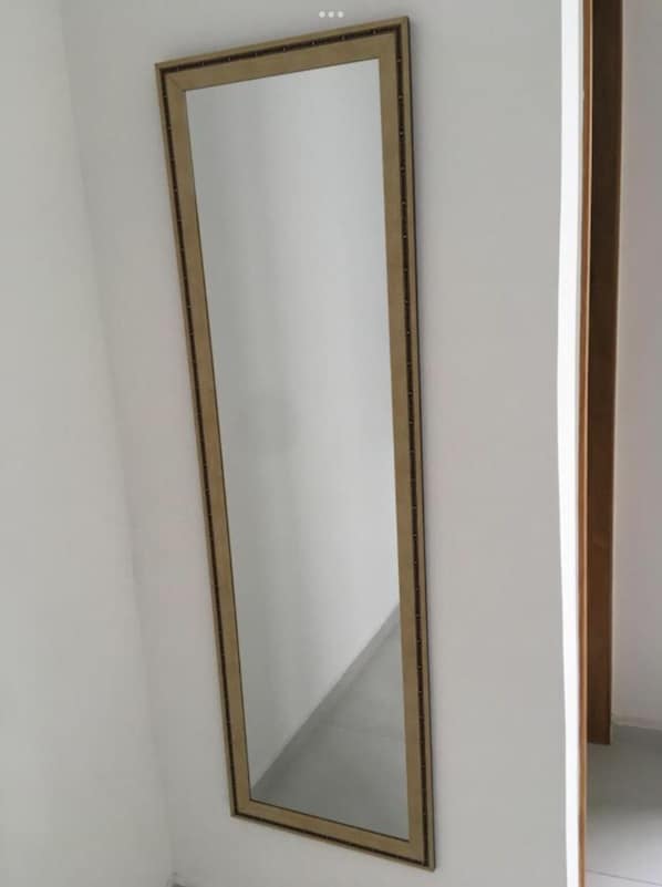 A tall, rectangular mirror with a simple, dark frame mounted on a plain white wall. - Hotel 34 (Guarulhos)