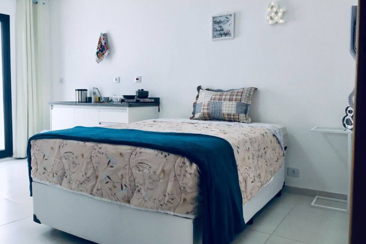 A bedroom with a bed, a small kitchenette, and a window with curtains.